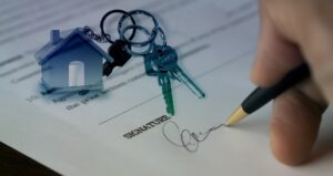 Man's hand signing a signuature with keys on the document